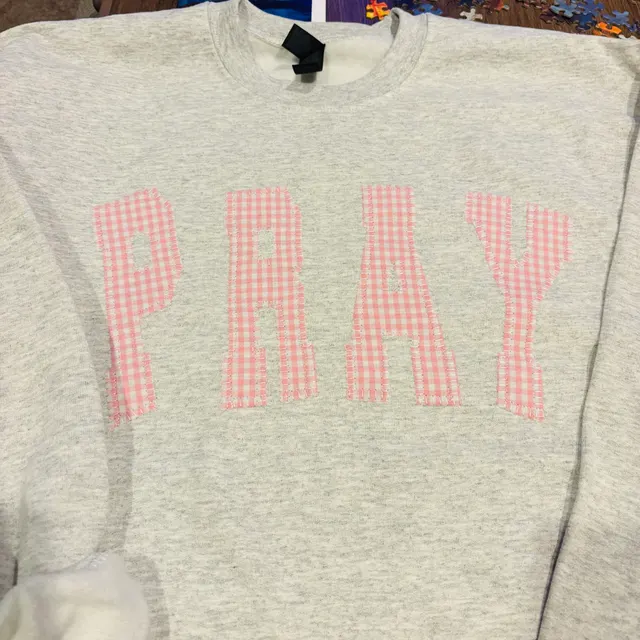 Heather grey crewneck with PRAY in frayed pink-and-white gingham appliqué letters