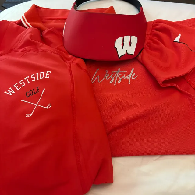 Red Westside Golf apparel set laid flat — a jacket with crossed clubs under WESTSIDE GOLF, a visor and a polo with the Westside script and W logo